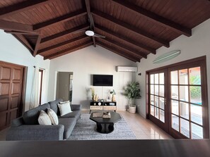 Een woonkamer met een hoge plafond, een flatscreen televisie aan de muur, een bank, een salontafel en een groot raam met uitzicht.