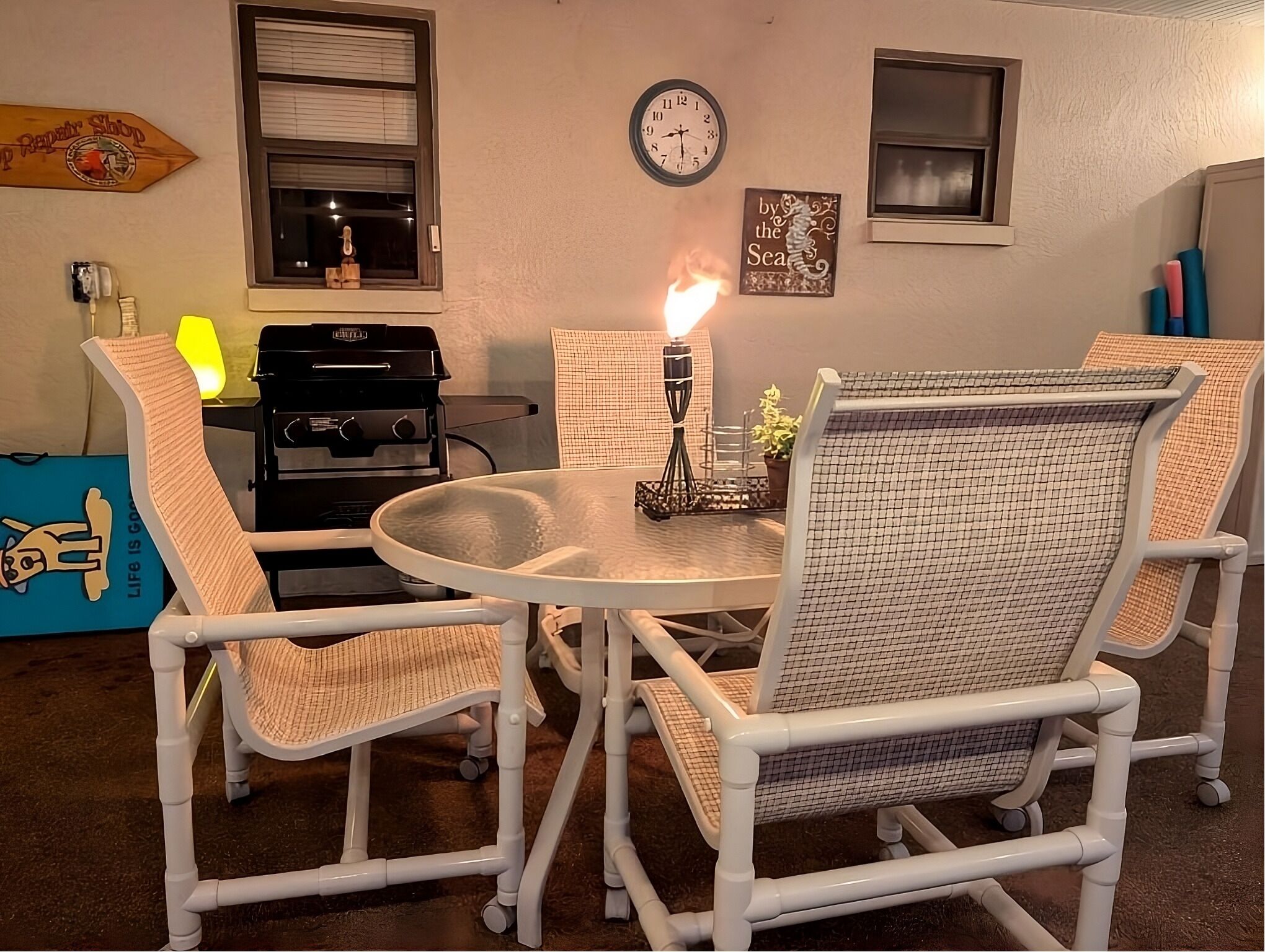 A dining area with a round table, four chairs, a clock, and a grill.