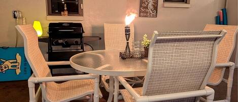 A dining area with a round table, four chairs, a clock, and a grill.