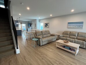 A modern living room with a staircase, a dining area, and a kitchen in the background. - Life is Better at the Beach! (Wildwood)