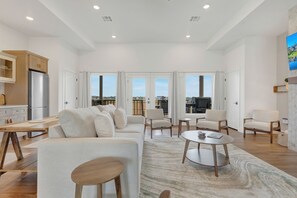 Uma sala de estar ampla com sofá, cadeiras, mesa de centro e cozinha equipada com geladeira.