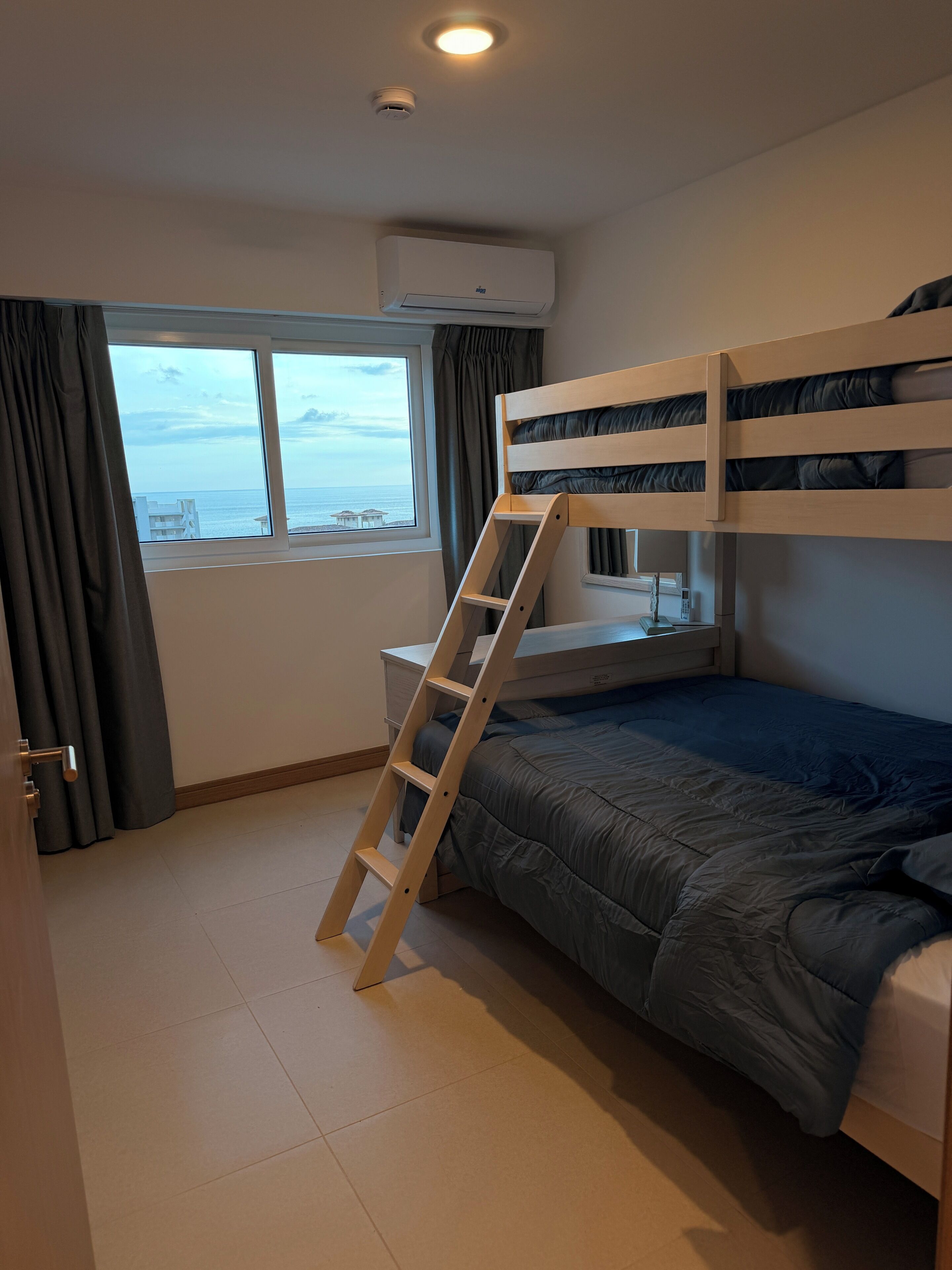A bedroom with a bunk bed, a ladder, a window with a view, and an air conditioning unit.