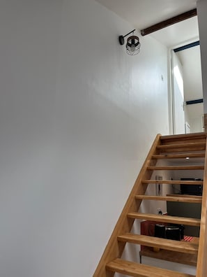 Un escalier en bois mène à une pièce équipée d’un téléviseur et d’appareils de cuisine.