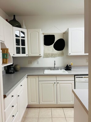 A kitchen with white cabinets, a built-in sink, and a decorative wall hanging. - Spacious 2BR Guest House - Perfect for Remote Work, Family and Pet-Friendly (Las Vegas)