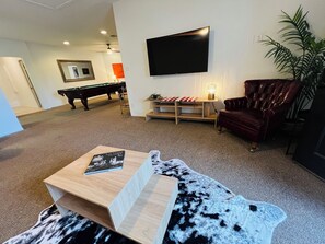 A living room with a pool table, a flat-screen TV mounted on the wall, a leather armchair, and a wooden coffee table with a book. - Spacious 2BR Guest House - Perfect for Remote Work, Family and Pet-Friendly (Las Vegas)