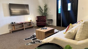 A living room with a flat-screen TV, a leather armchair, a sofa, a coffee table, a plant, and a door with a window. - Spacious 2BR Guest House - Perfect for Remote Work, Family and Pet-Friendly (Las Vegas)