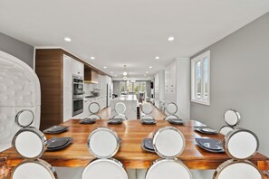 Una cocina moderna con armarios blancos, una isla central y un comedor con mesa y sillas de madera.