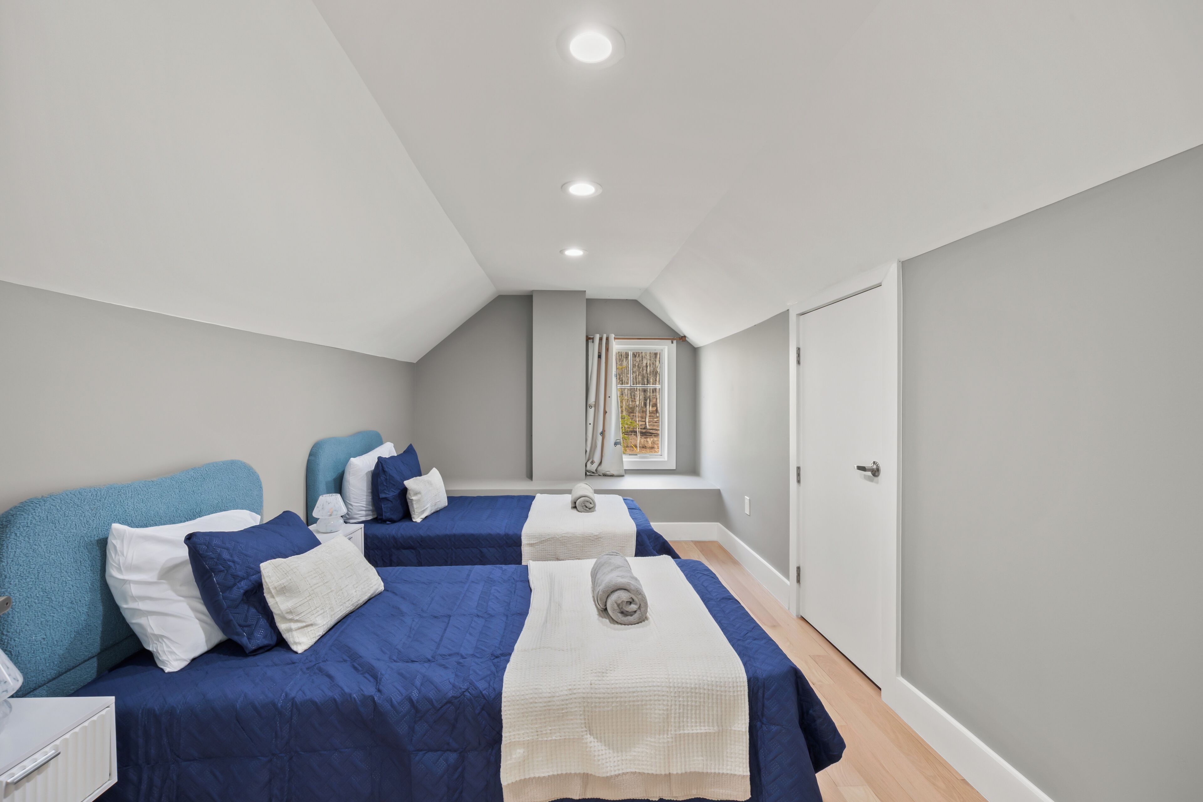 A bedroom with two beds, a window with curtains, a door, and a ceiling light.