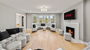 A modern living room with a sectional sofa, ottomans, a fireplace, and a TV displaying 'NETFLIX'. - Grand 8BR Estate w/ Game Room (Morristown)
