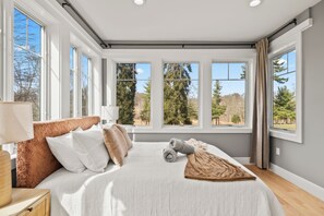 Un dormitorio con una cama grande, varias ventanas y vistas a árboles.