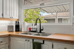 Eine Küche mit weißen Schränken, einer Holzausziehtafel, einem schwarzen Wasserhahn und einem Fenster mit Blick auf einen Baum.