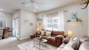 A living room with a brown sofa, a coffee table, and a dining area with a wooden table and chairs. - *New* Ducks & Diamonds 3br/3bath (Bryan)