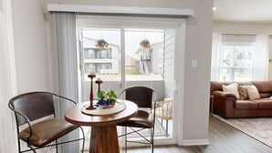 A living room with a brown leather sofa, a round wooden table with chairs, and a sliding glass door leading to a balcony. - *New* Ducks & Diamonds 3br/3bath (Bryan)