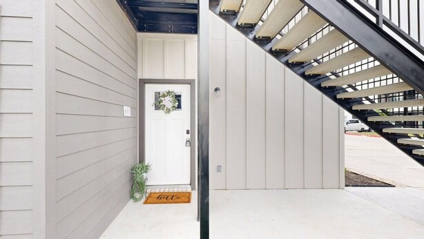 A modern building entrance with a white door, a doormat, and a staircase. - *New* Ducks & Diamonds 3br/3bath (Bryan)