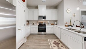 A kitchen with white cabinets, stainless steel appliances, and a wooden floor. - *New* Ducks & Diamonds 3br/3bath (Bryan)