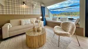 Een moderne woonkamer met een bank, een rond salontafel, een zachte fauteuil en uitzicht op bergen door grote ramen.