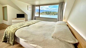 Een slaapkamer met een groot bed, een televisie op een standaard en uitzicht op een meer en bergen.