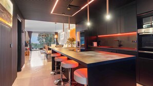 A modern kitchen with a long island, bar stools, pendant lighting, and a view to the outdoors.
