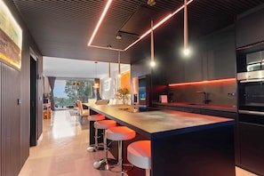 A modern kitchen with a long island, bar stools, pendant lighting, and a view to the outdoors. - VIP Al Fattah Luxury (Estepona)
