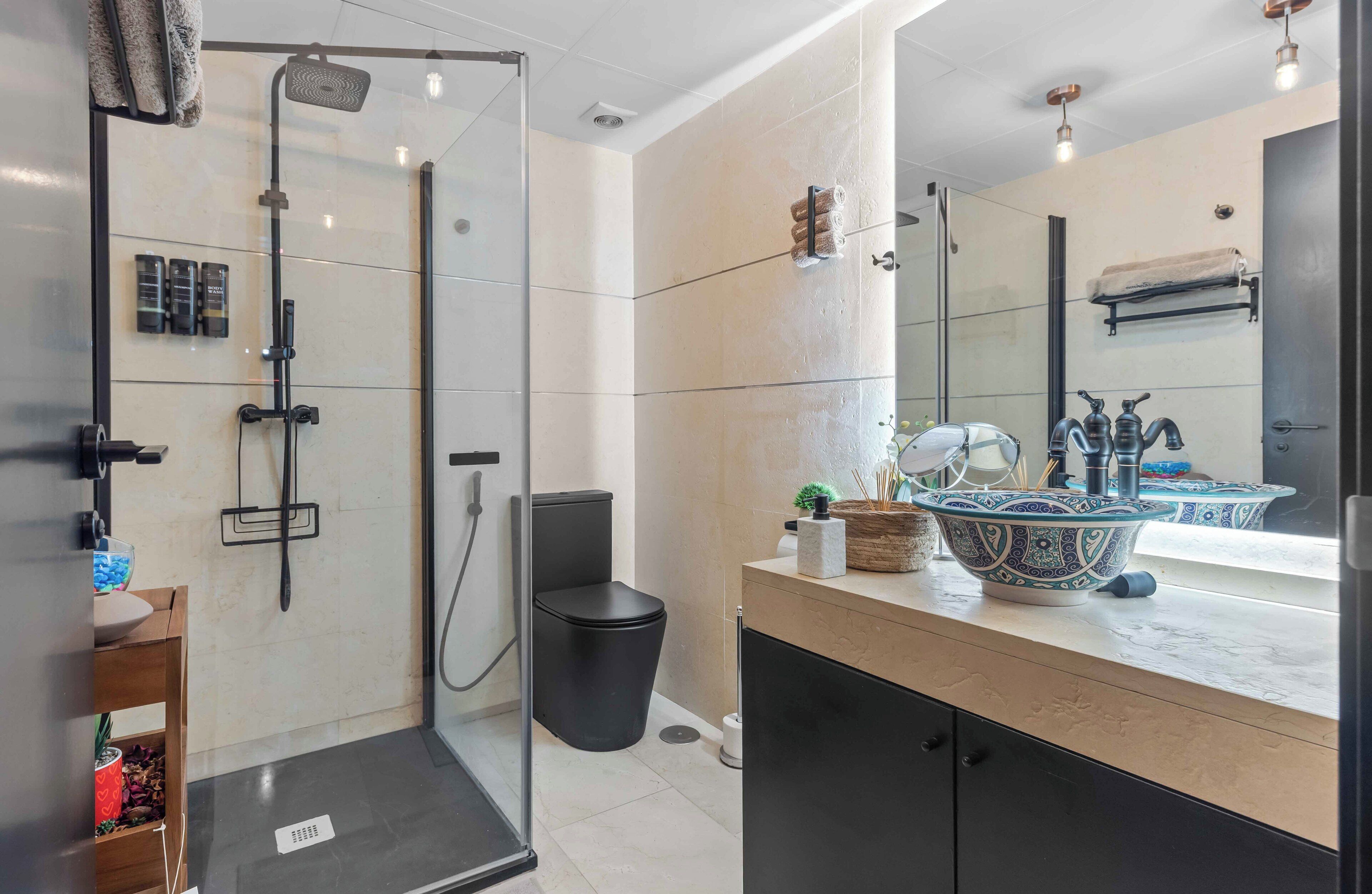 Une salle de bain moderne avec une douche à parois de verre, des toilettes noires, un meuble-lavabo agrémenté d’un décor et un miroir.