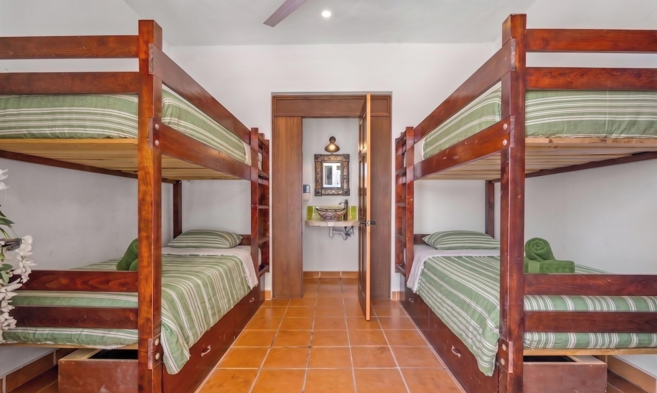 A room with four bunk beds, a small bathroom with a mirror, and a tiled floor.
