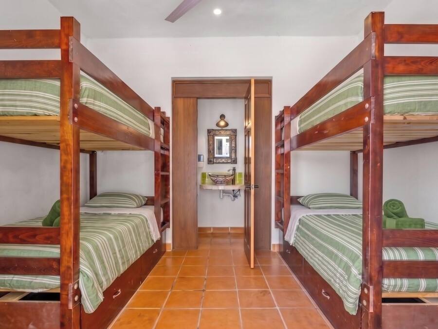 A room with four bunk beds, a small bathroom with a mirror, and a tiled floor.