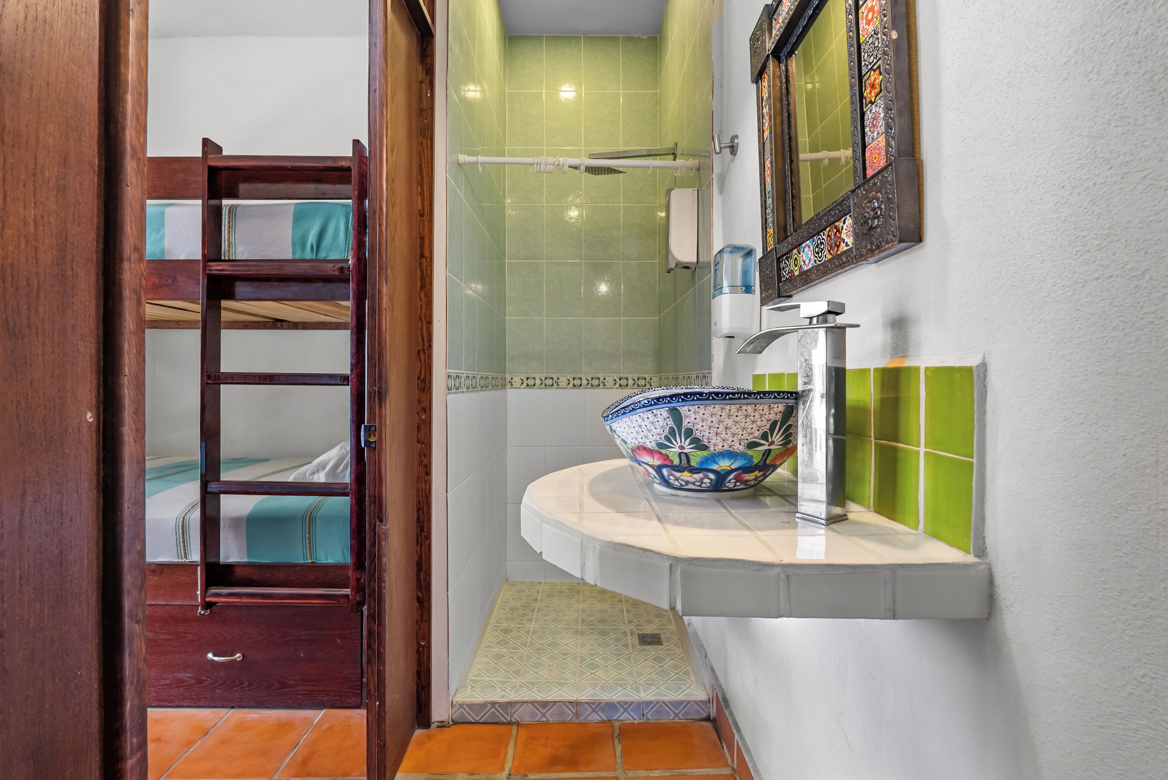 Un baño con ducha, un lavamanos con un cuenco decorativo, una escalera de madera que lleva a una litera y un escalón que da a la ducha.