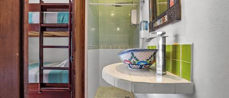 Un baño con ducha, un lavamanos con un cuenco decorativo, una escalera de madera que lleva a una litera y un escalón que da a la ducha.