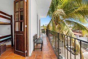 Een balkon met een houten deur, een bankje en uitzicht op palmbomen en gebouwen.