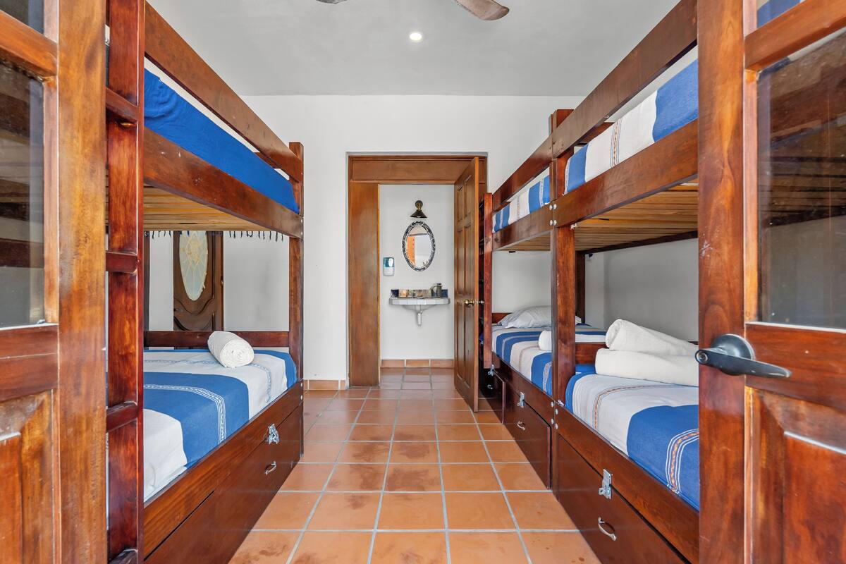 A corridor with bunk beds, a mirror, a sink, and a door leading to another room.