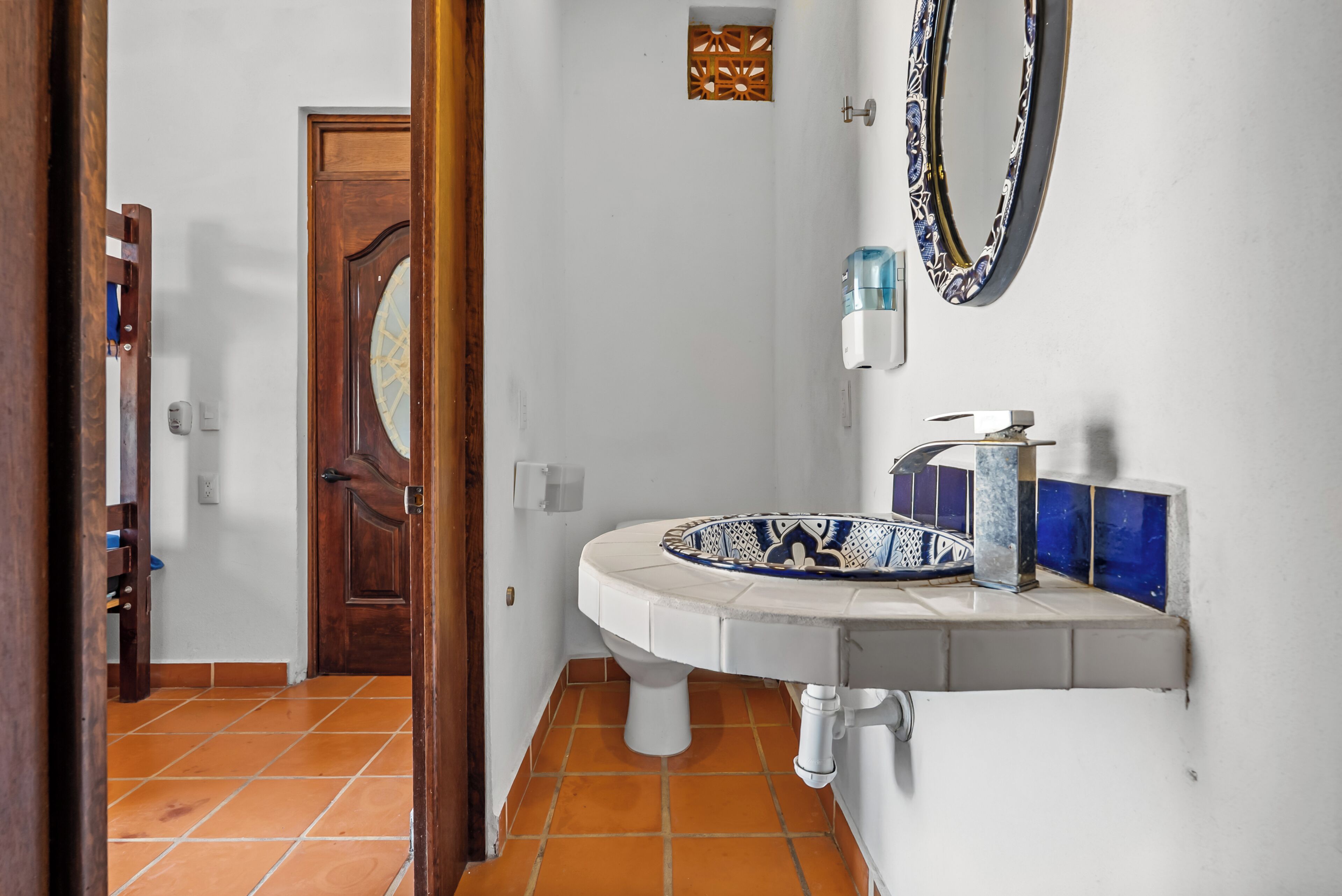 Une salle de bain avec un lavabo blanc, un miroir et une porte donnant sur une autre pièce.
