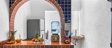 A kitchen with a tiled backsplash, a water dispenser, a blender, and a fruit bowl.