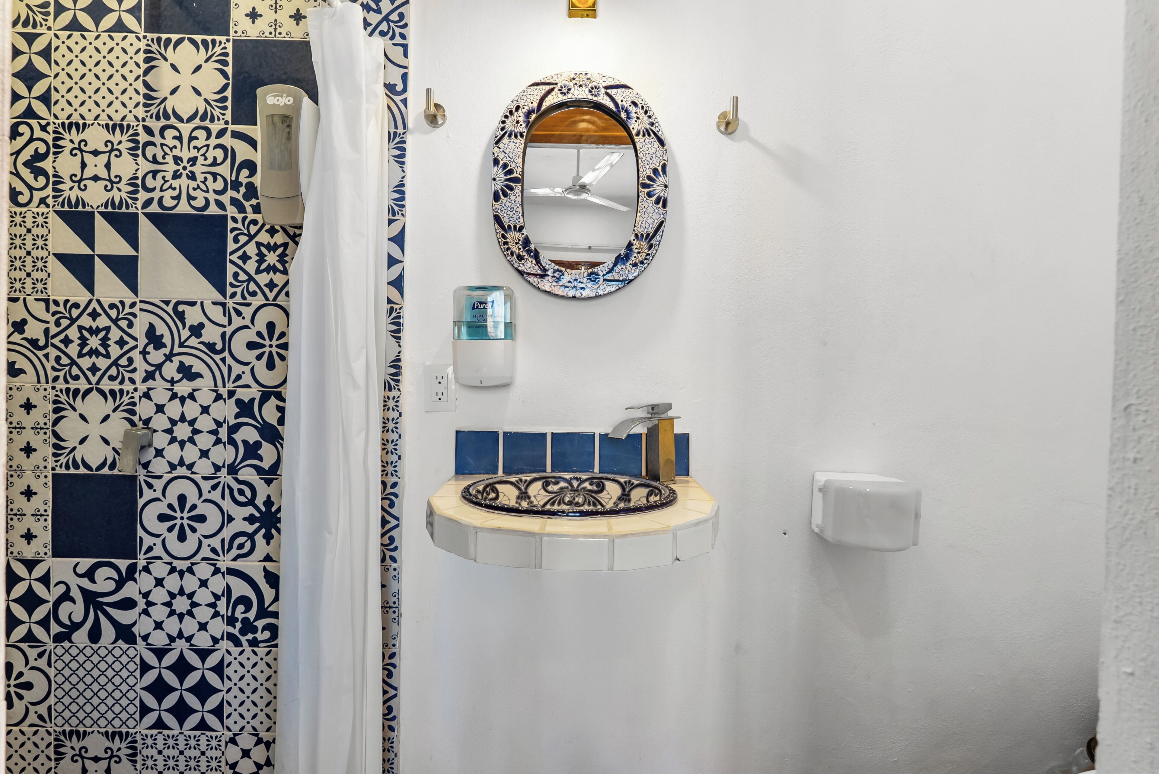 A bathroom with a patterned tile wall, a mirror with a decorative frame, a sink with a soap dispenser, and a towel rack.