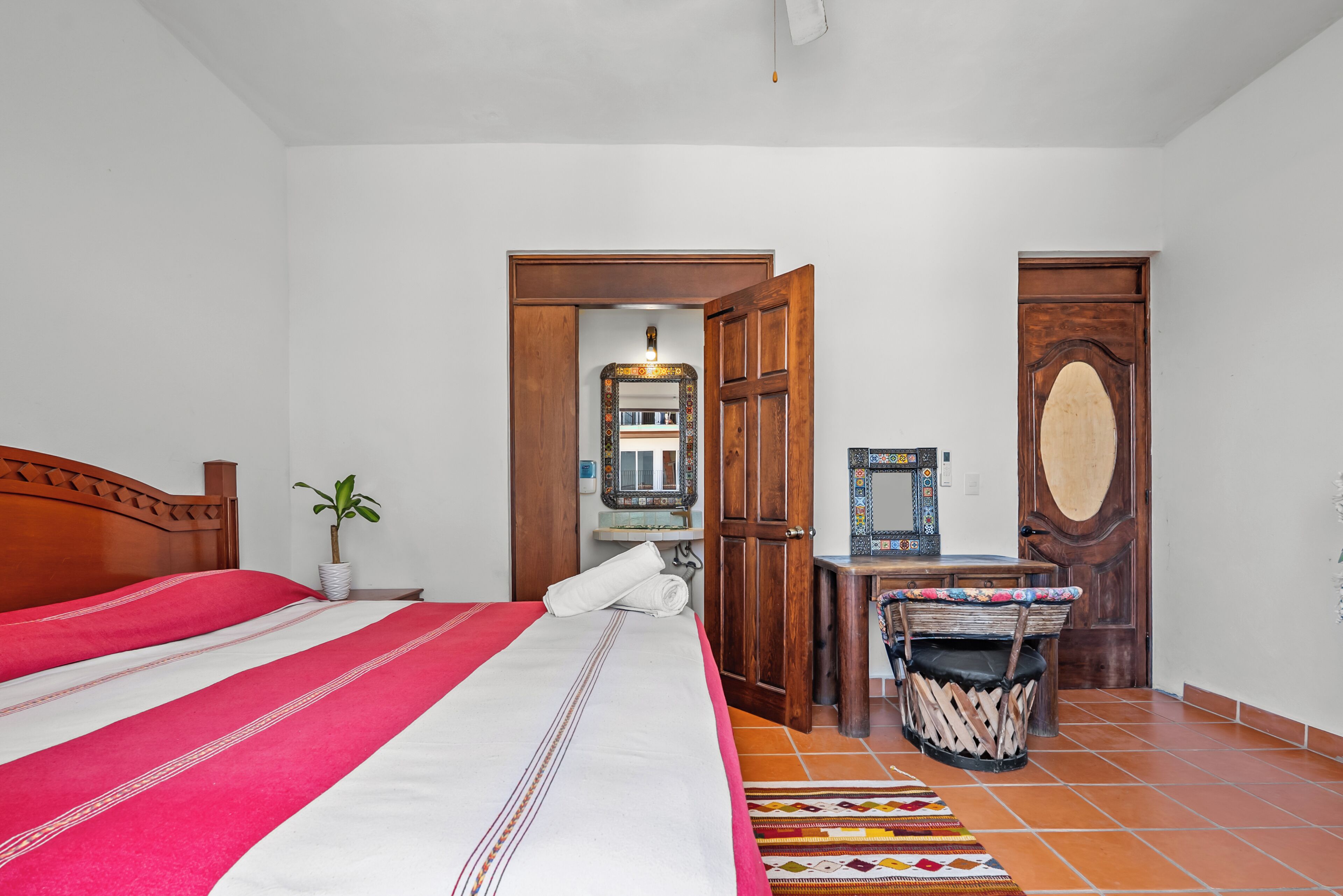 A bedroom with a bed, a wooden door, a small table, and a chair.