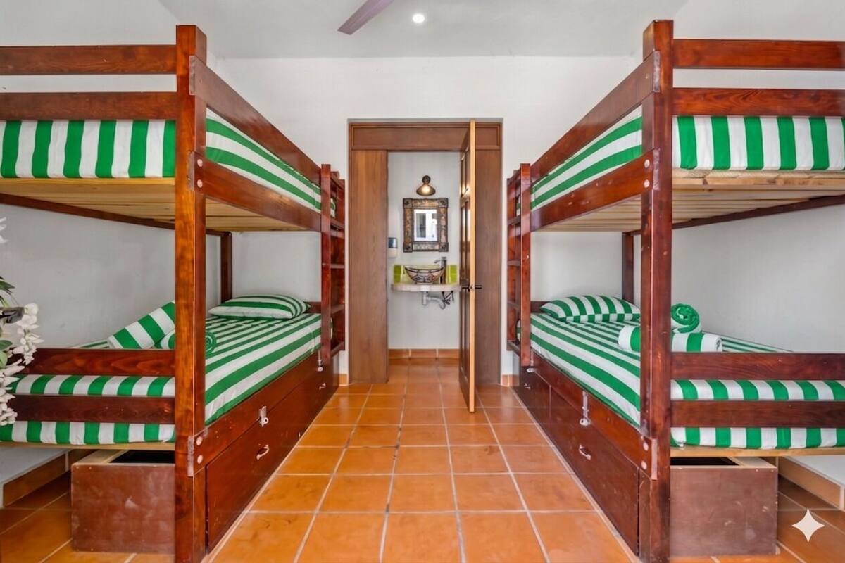 A room with four bunk beds, each with a green and white striped mattress, arranged in a corridor.