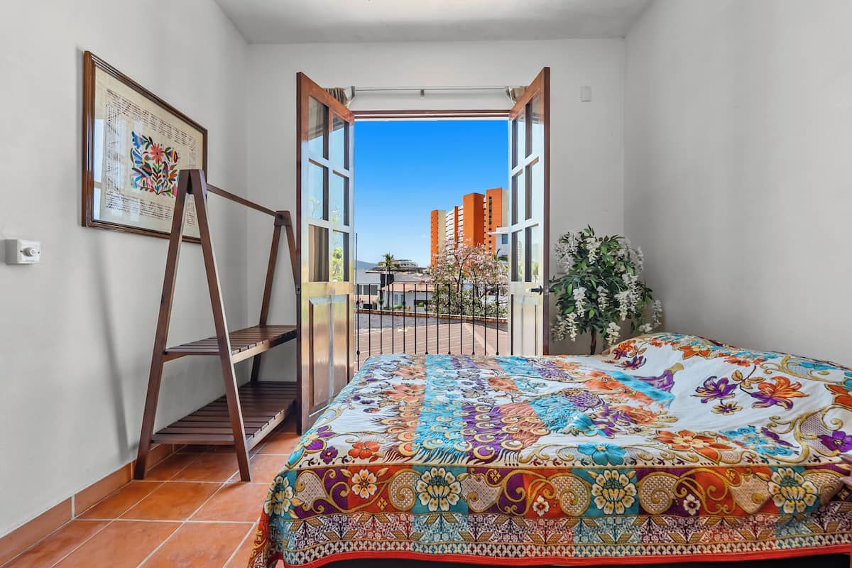Un dormitorio con cama, escalera, ventana y una obra de arte enmarcada en la pared.