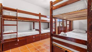 Um quarto com quatro beliches de madeira, cada um com colchão e almofadas, e piso de azulejos.