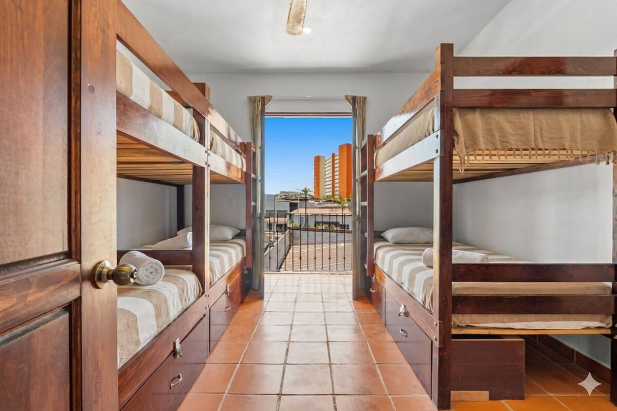 A room with bunk beds, a tiled floor, a door with a brass handle, and a view of buildings outside.