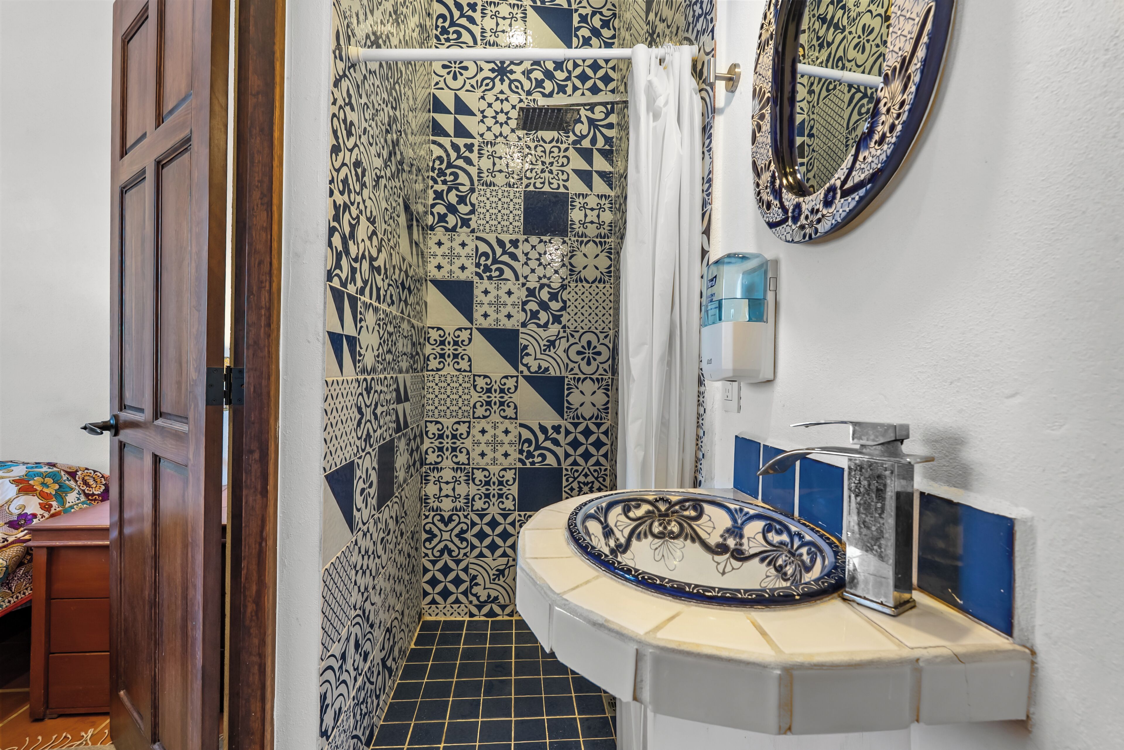 A bathroom with patterned tiles, a sink with a decorative basin, a mirror, and a shower area.