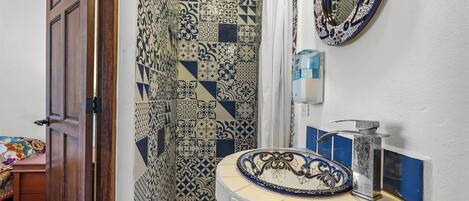 A bathroom with patterned tiles, a sink with a decorative basin, a mirror, and a shower area.