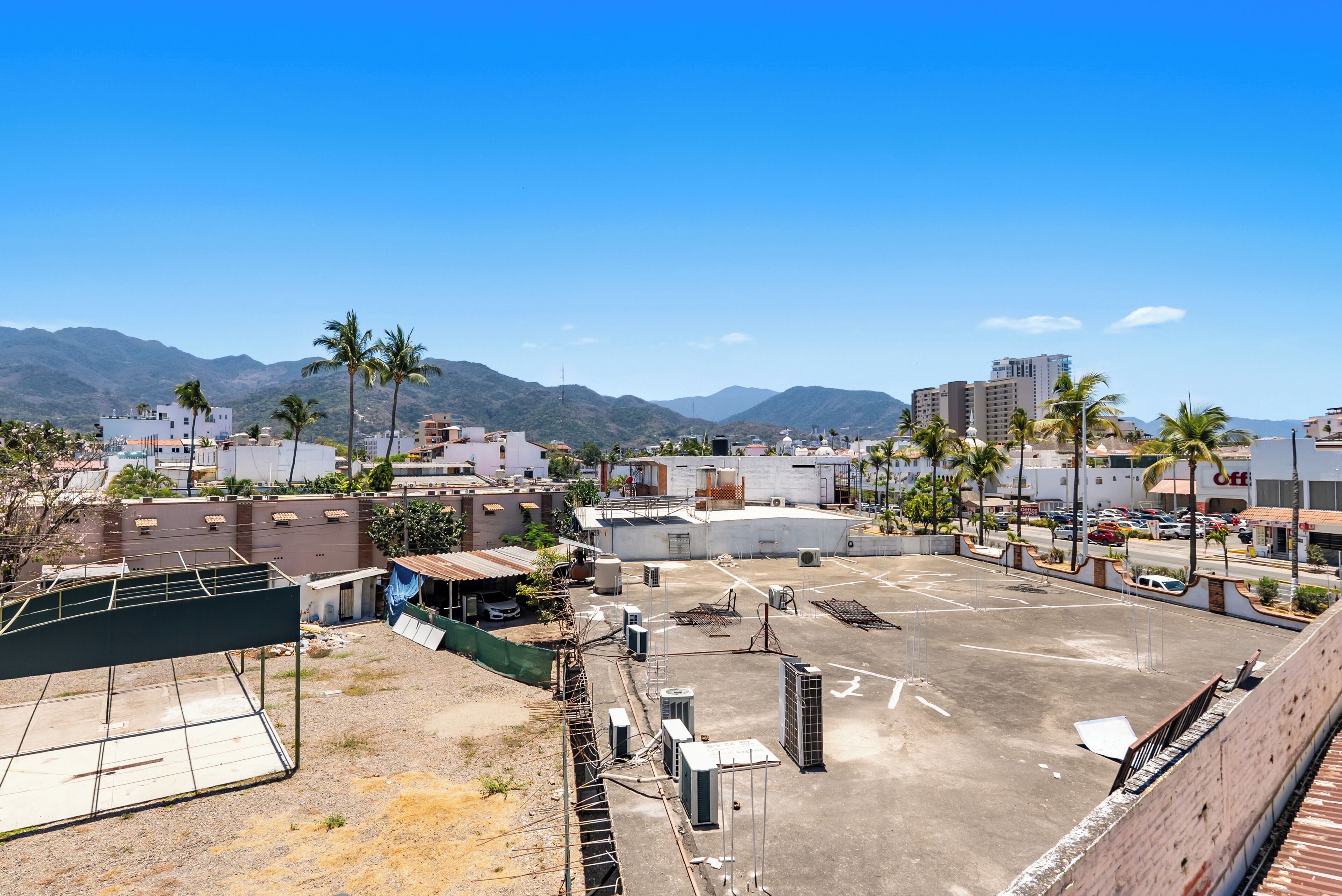 A rooftop parking area with buildings, palm trees, and mountains in the background.