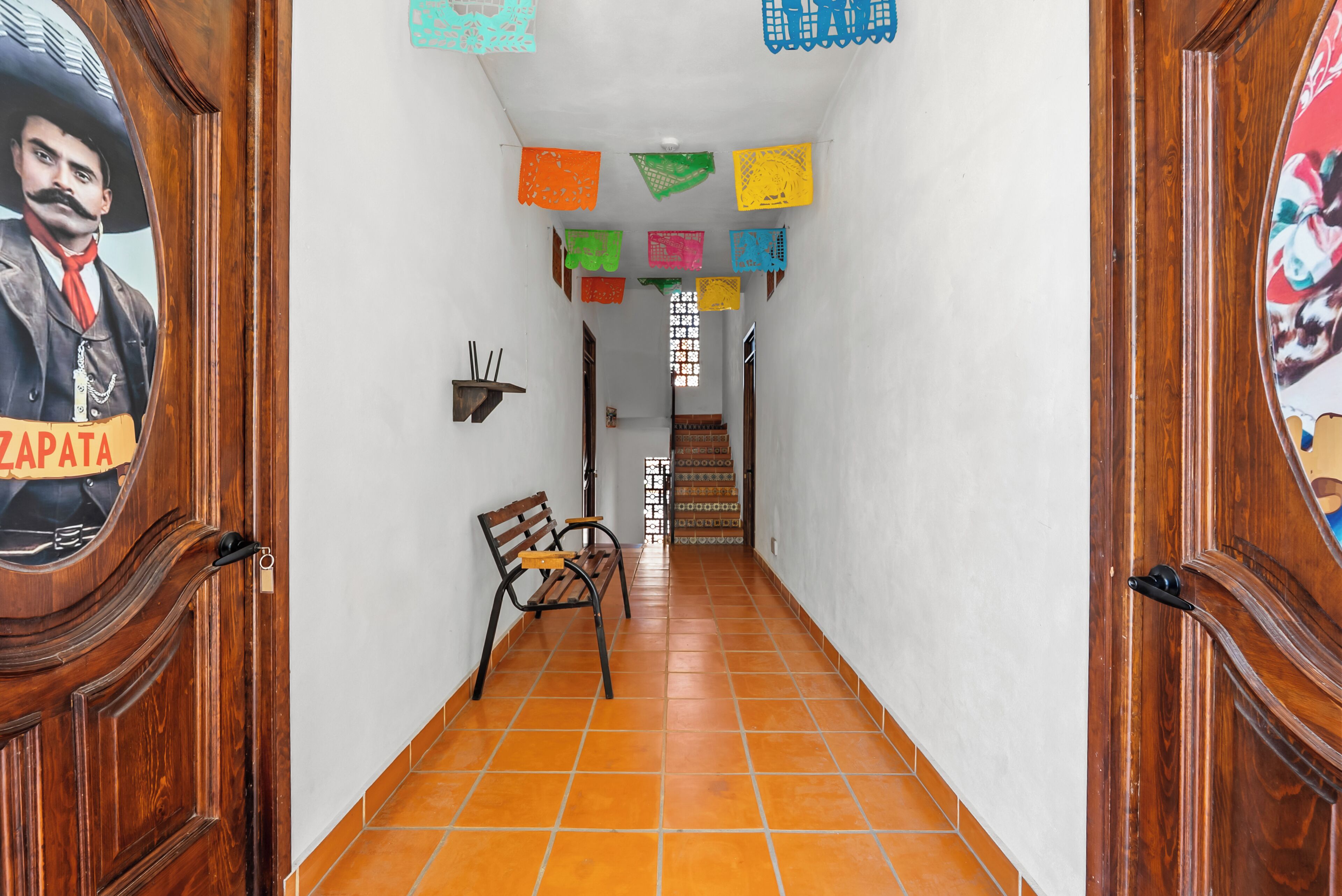 Un pasillo con una puerta de madera a la izquierda, un banco en el centro y una escalera al final.