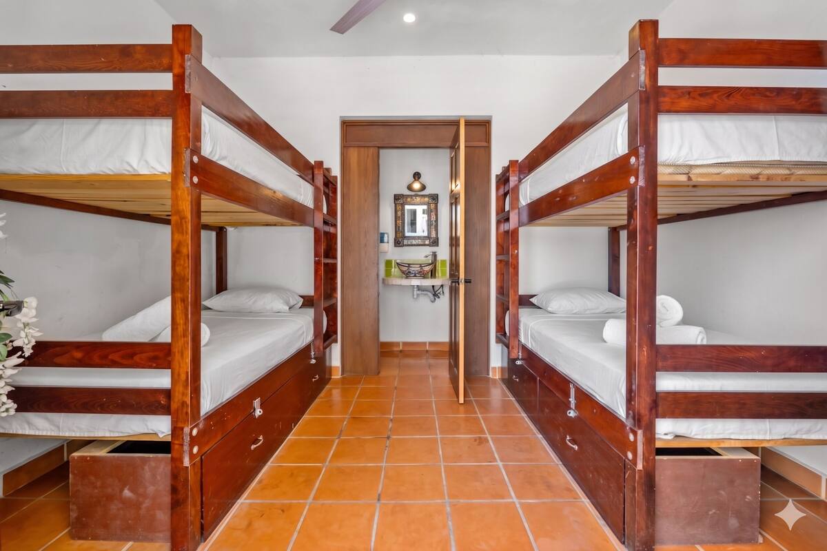A room with two wooden bunk beds, a tiled floor, a small mirror, and a door leading to another room.