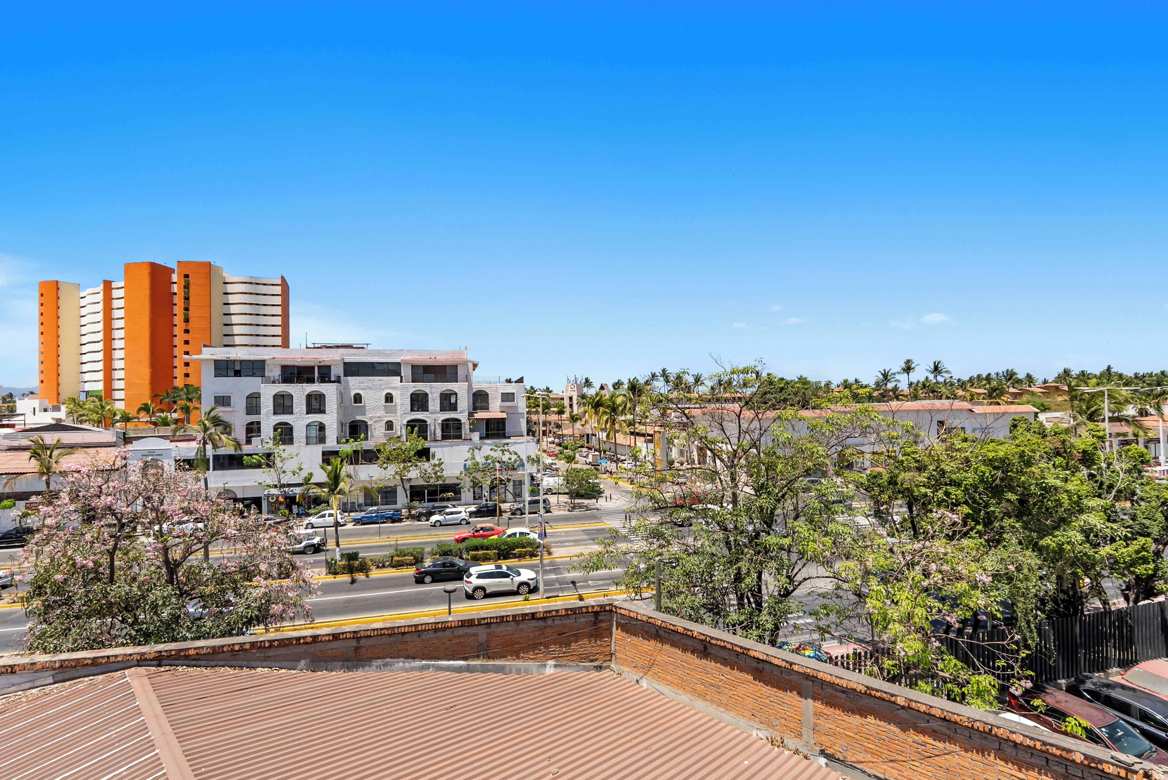 A view of a cityscape with modern buildings, a street with cars, and trees.