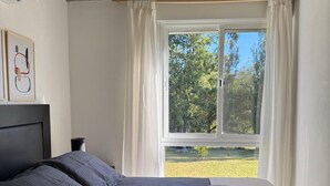 A bedroom with a bed, a window with curtains, a headboard, and a framed picture on the wall.