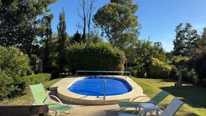 An outdoor swimming pool with a diving board, surrounded by green chairs and lush greenery.
