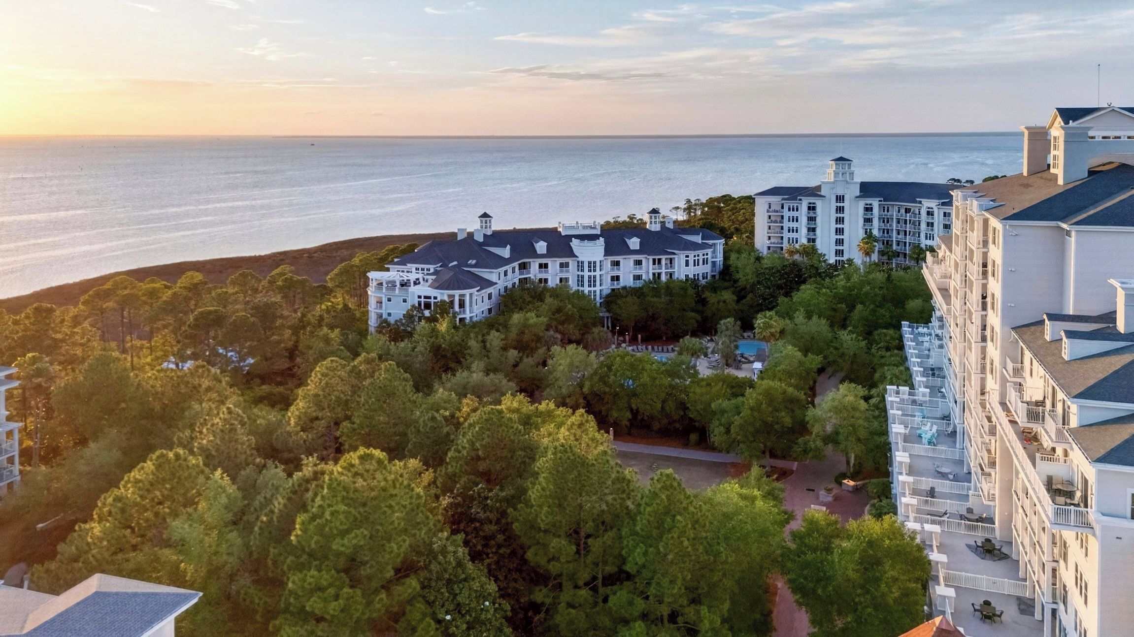 A large resort with multiple buildings, a swimming pool, and a view of the ocean.