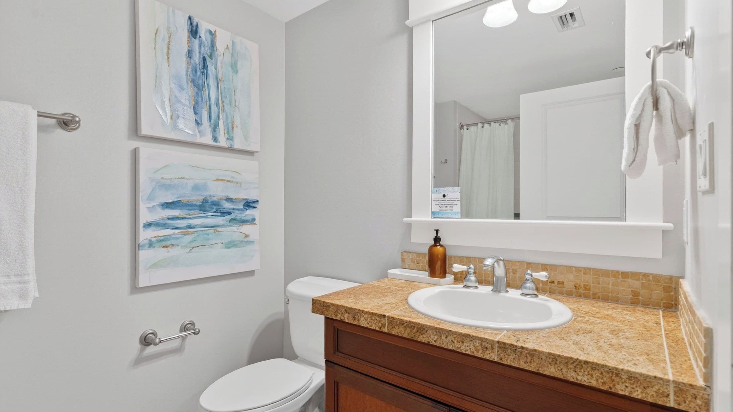 A bathroom with a white toilet, a sink with a beige countertop, and two wall-mounted paintings.