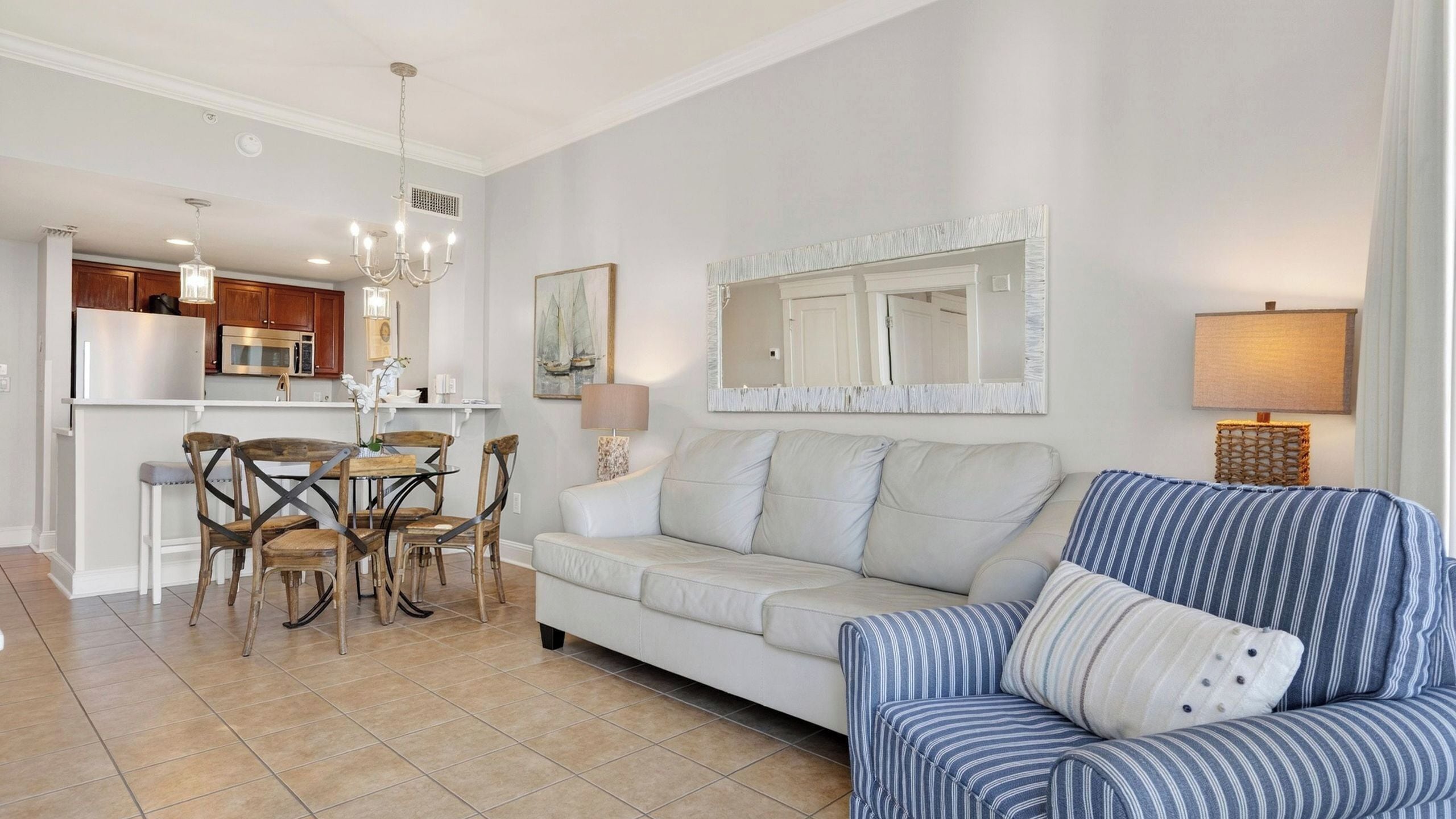 Un salon moderne comprenant un canapé, un fauteuil à rayures, une table à manger avec des chaises, un coin cuisine et un grand miroir.