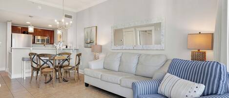 Un salon moderne comprenant un canapé, un fauteuil à rayures, une table à manger avec des chaises, un coin cuisine et un grand miroir.